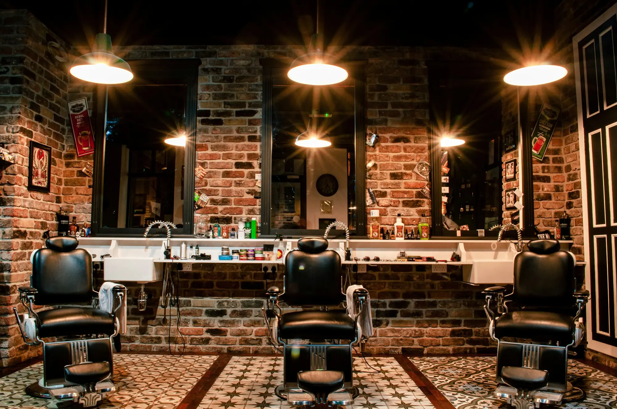 A barbershop interior with leather chairs against a bare brick wall under warm pendant lights