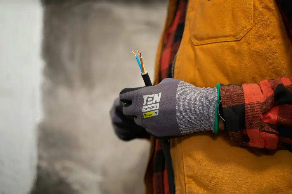 A gloved hand holding twin and earth cable against a bare wall
