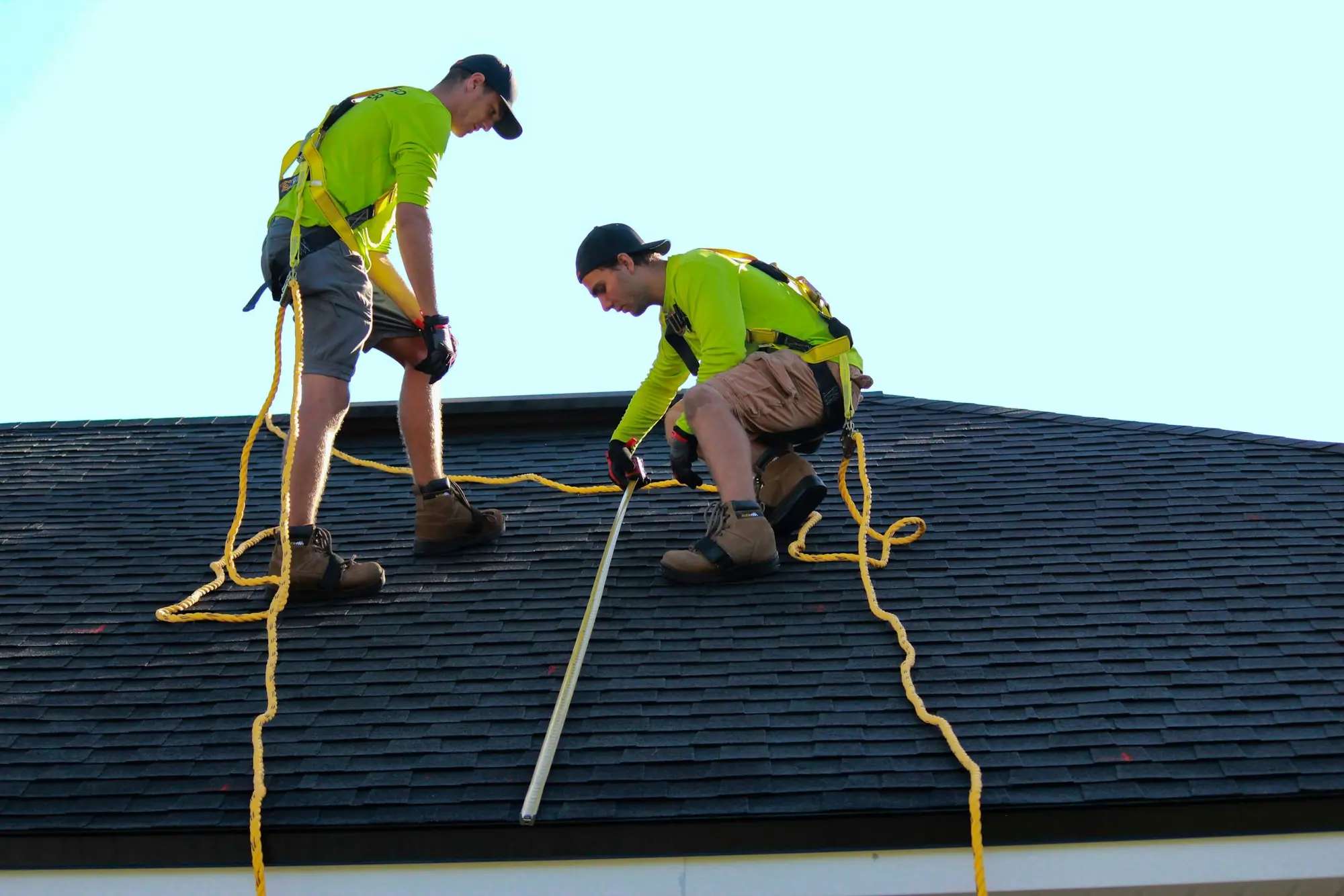 Two roofers working on a roof slope with safety lines