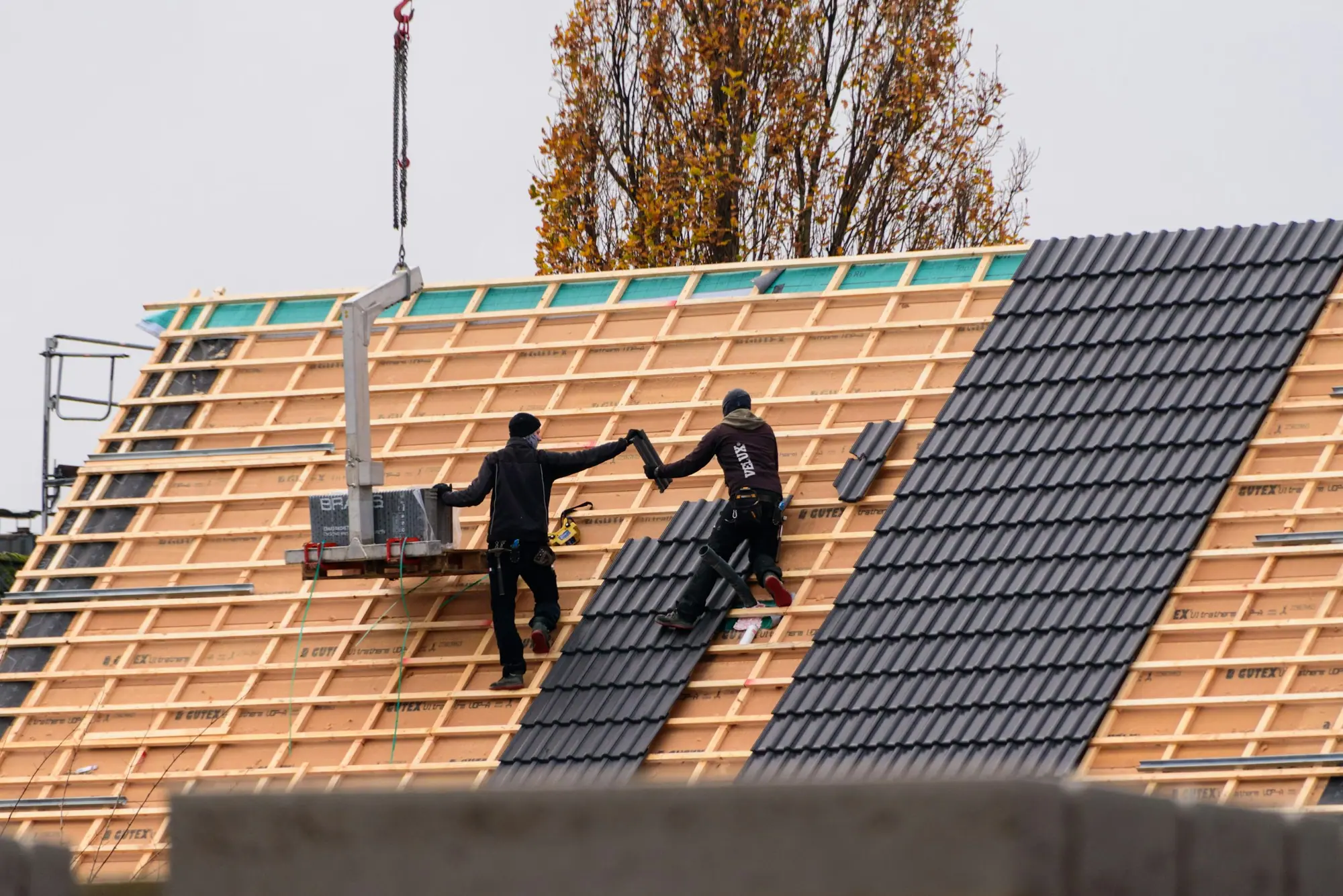 Roofers laying interlocking tiles on battens across a new roof